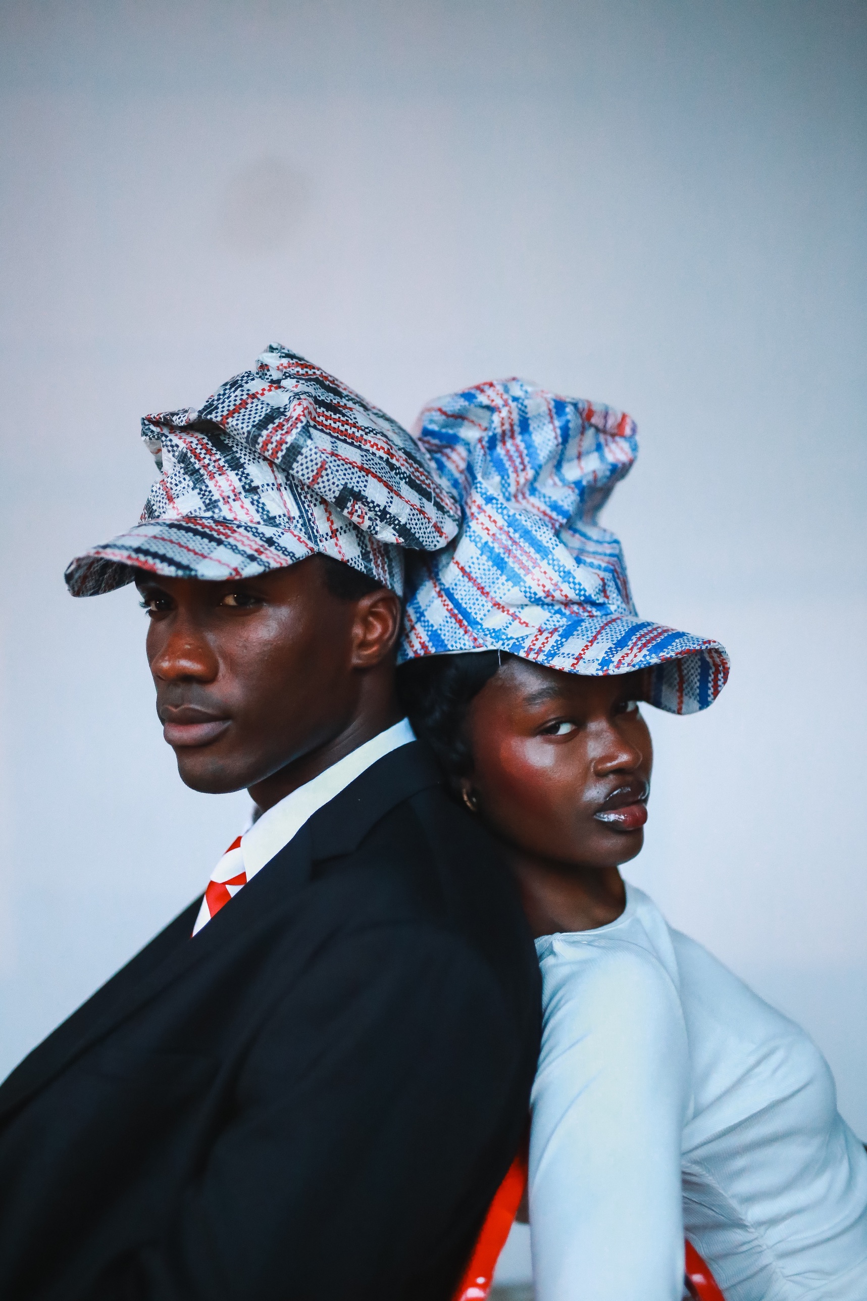 Two models back to back in close-up, both wearing Homecoming Hats in Ghana Must Go bag textile