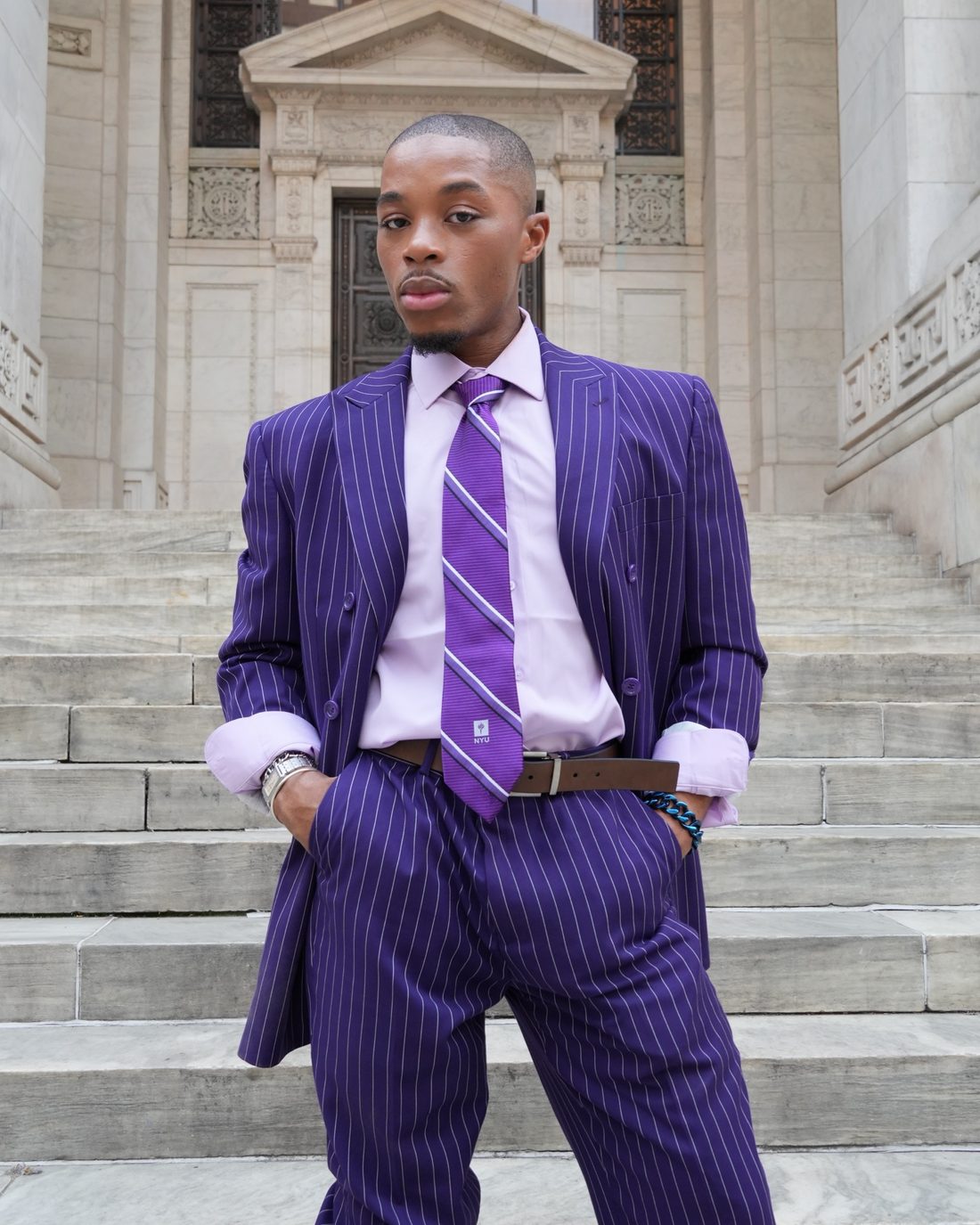 Richmond Addae in a purple pinstripe suit on stone library steps